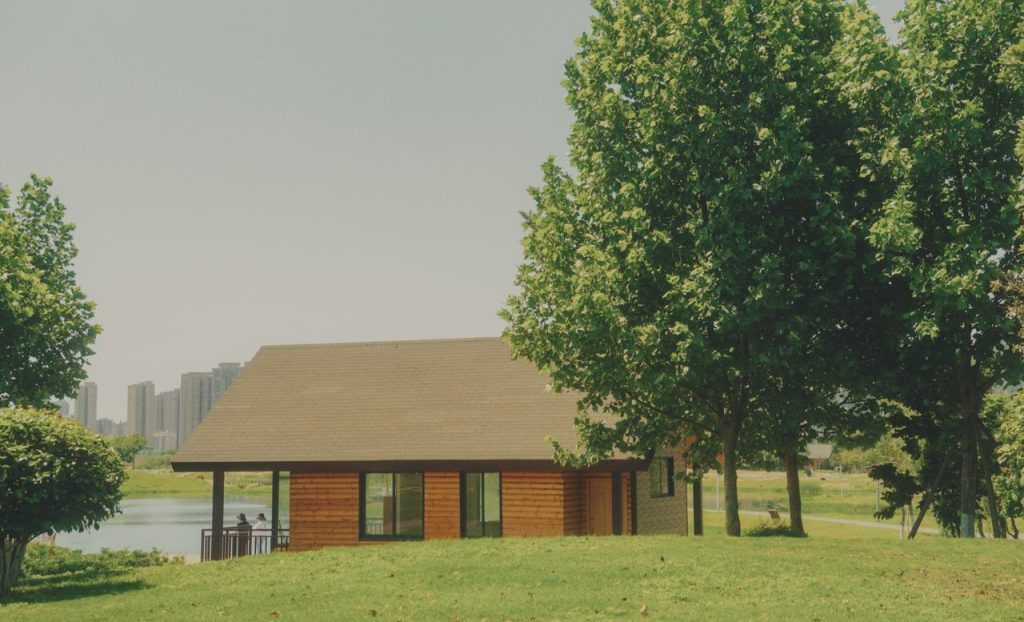 Charming rural cottage amidst lush greenery with a city skyline backdrop.